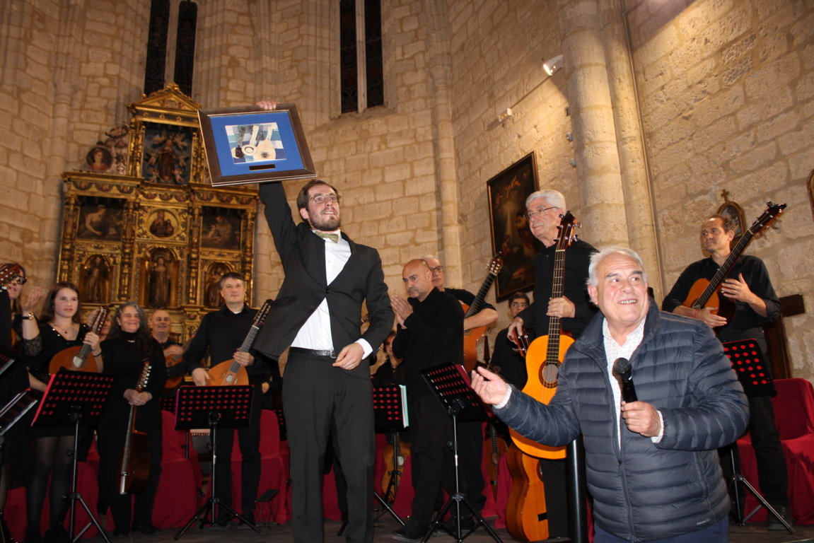 Músicos con instrumentos de cuerda acompañan a un hombre que sostiene un cuadro en alto.