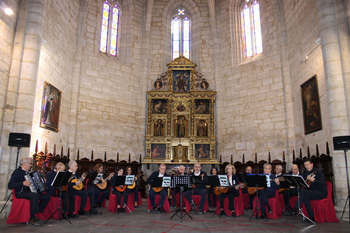 Músicos de una agrupación de plectro actúan sentados ante el retablo de una iglesia.