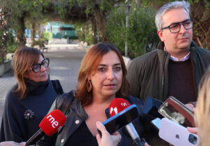 Una mujer habla ante varios micrófonos mientras otras personas la acompañan.