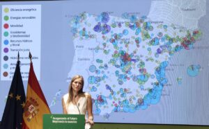 Mujer habla ante un mapa de España con indicadores de energía y dos banderas