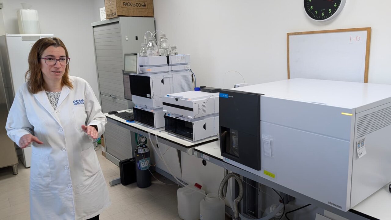 Mujer con bata blanca junto a equipos de análisis en un laboratorio.