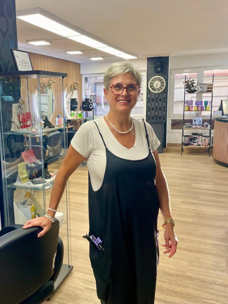 Mujer con gafas y delantal negro posa en el interior de una peluquería.