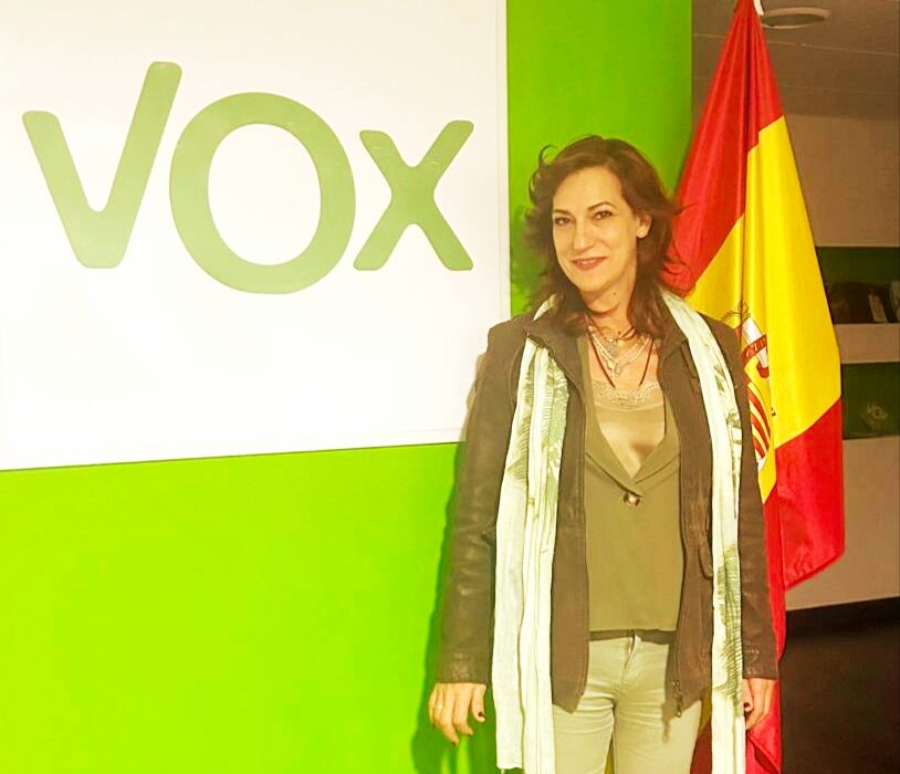 Mujer de pie junto a un cartel de VOX y una bandera española.