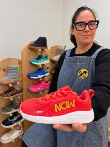 Mujer sostiene una zapatilla roja Naw frente a una exposición de calzado.