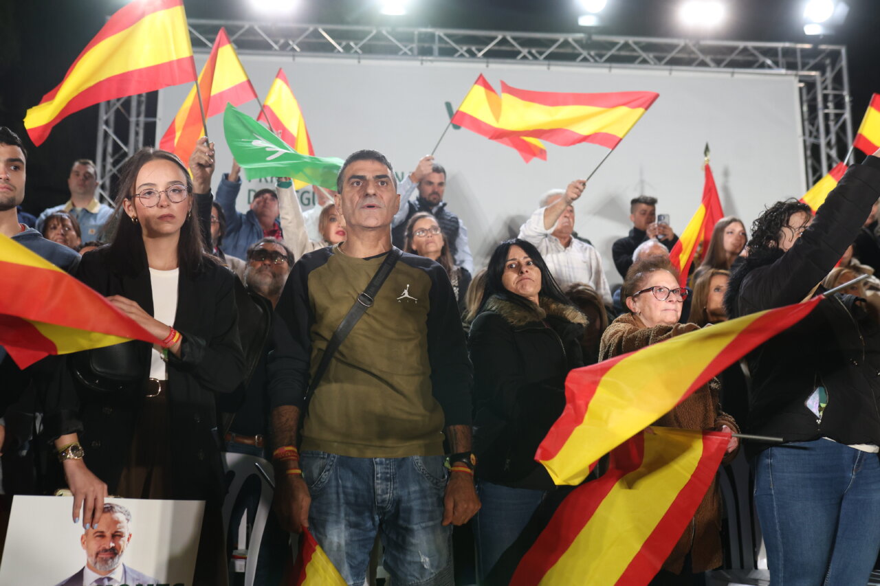 Varias personas sostienen banderas españolas entre la multitud en un acto político.