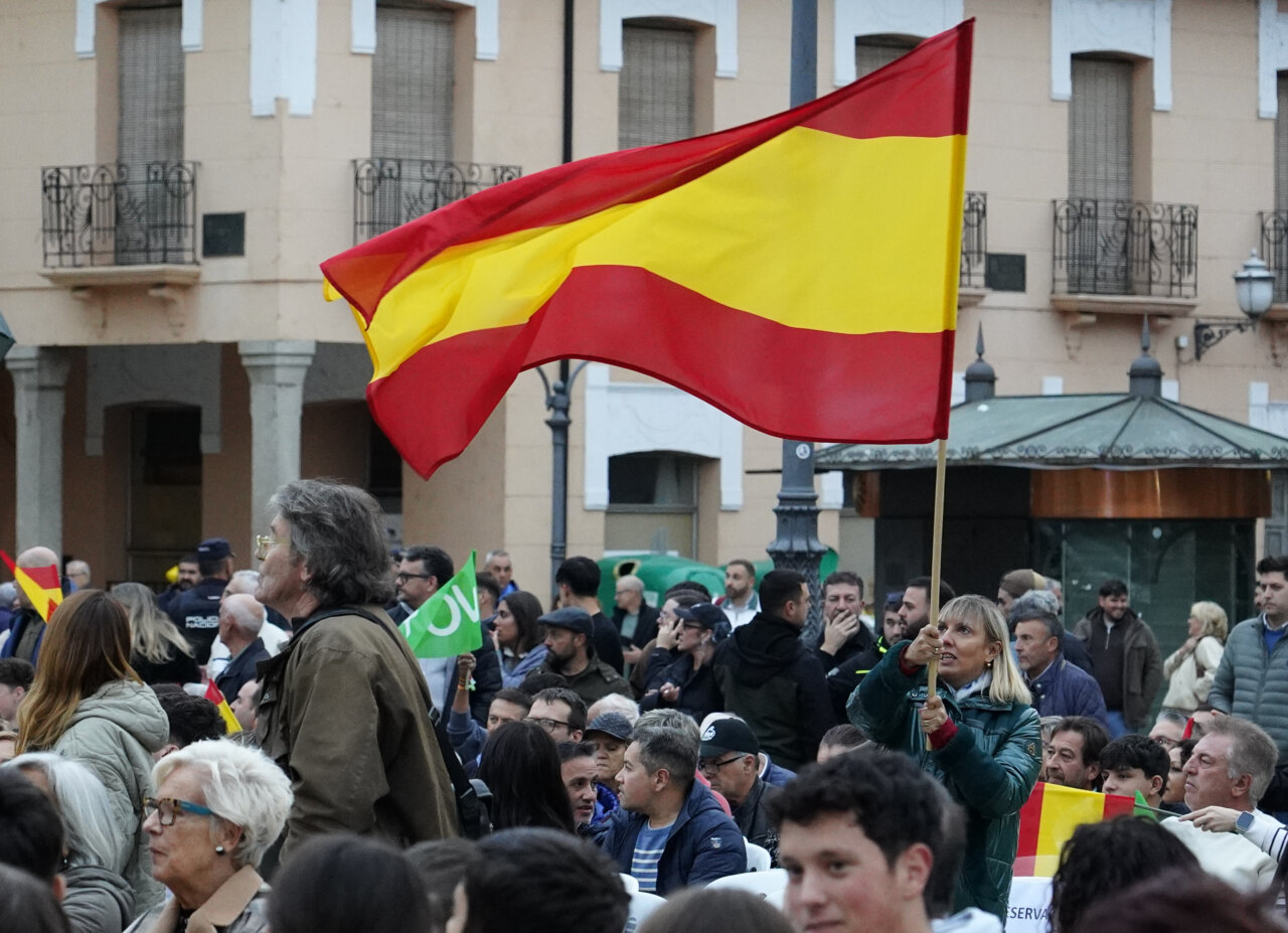 Una multitud sostiene banderas españolas y una bandera verde de Vox en una plaza.