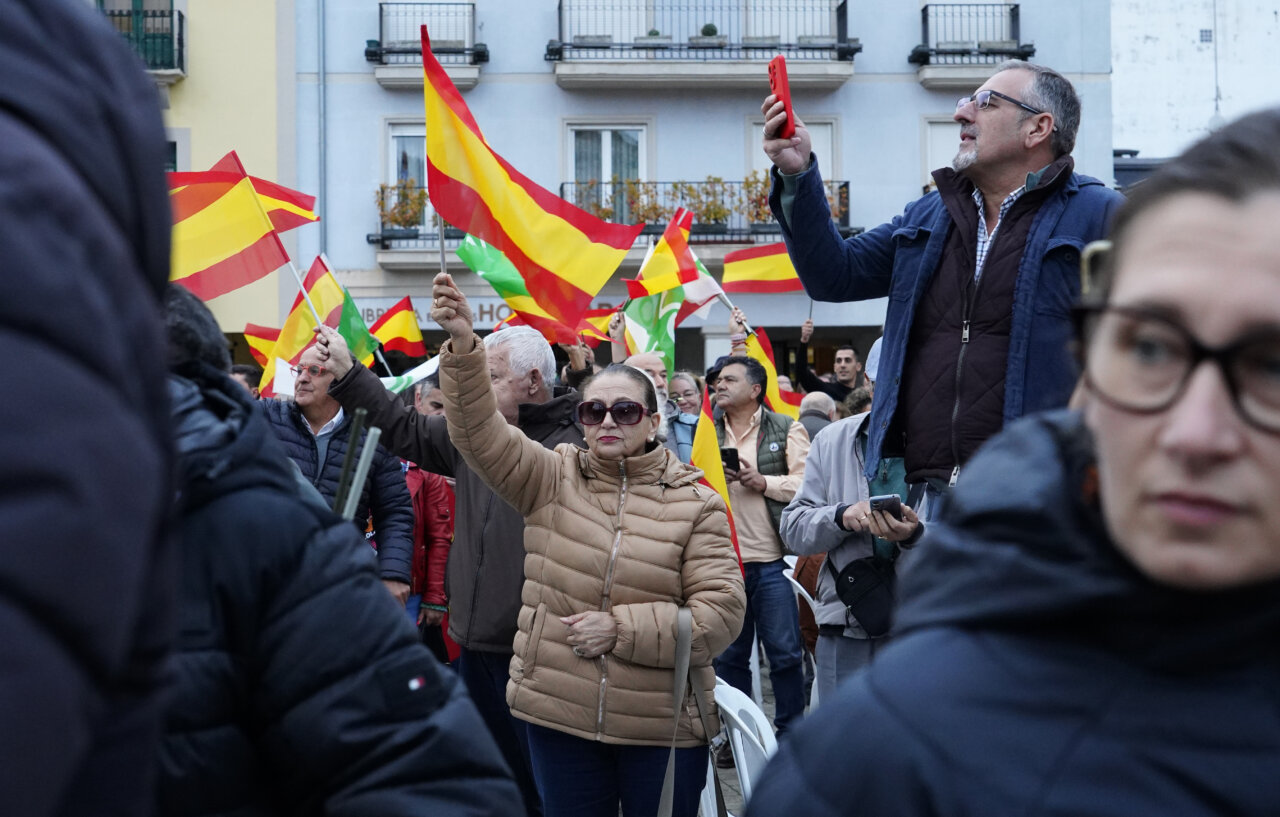 Varias personas sostienen banderas españolas entre una multitud reunida en una calle.