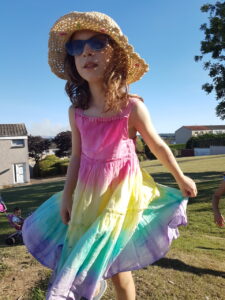 Niña con vestido colorido, sombrero tejido y gafas de sol en un jardín.