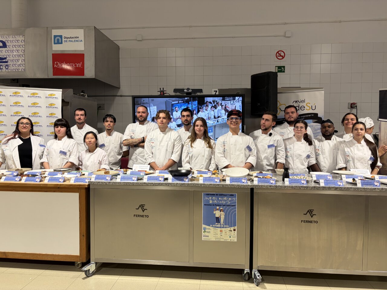 Grupo de participantes con chaquetas blancas posa detrás de un mostrador en una cocina.