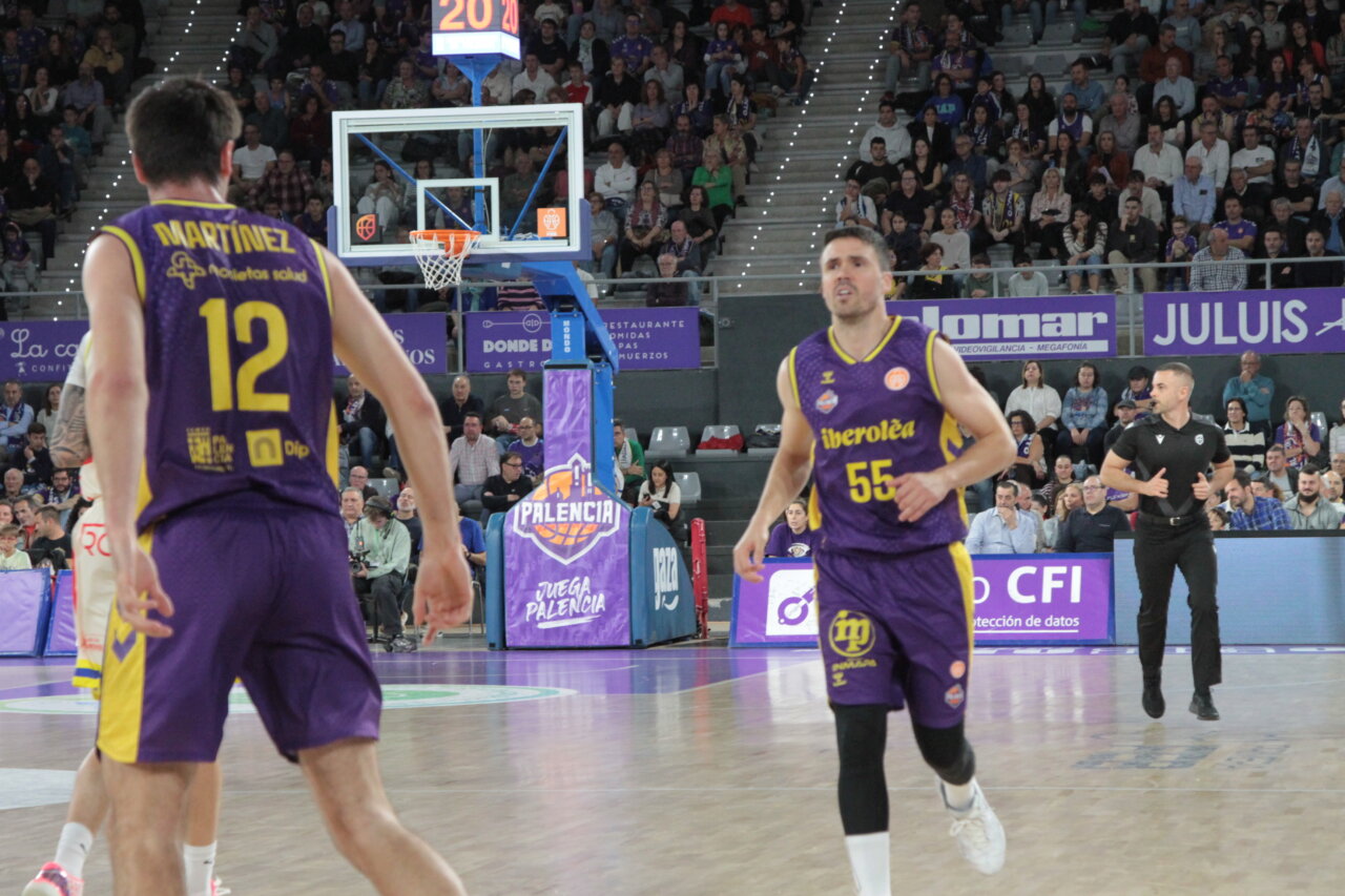 Dos jugadores de baloncesto con uniforme morado y amarillo durante un partido en una cancha cubierta.