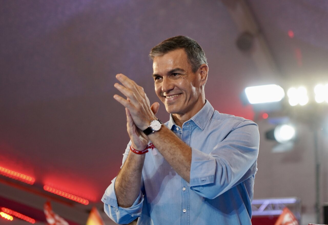 Pedro Sánchez sonríe y aplaude bajo luces de escenario.
