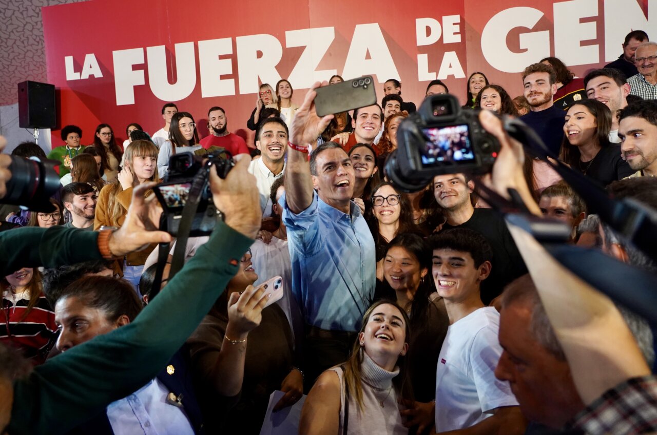 Pedro Sánchez posa para una foto con asistentes frente a un cartel de campaña.