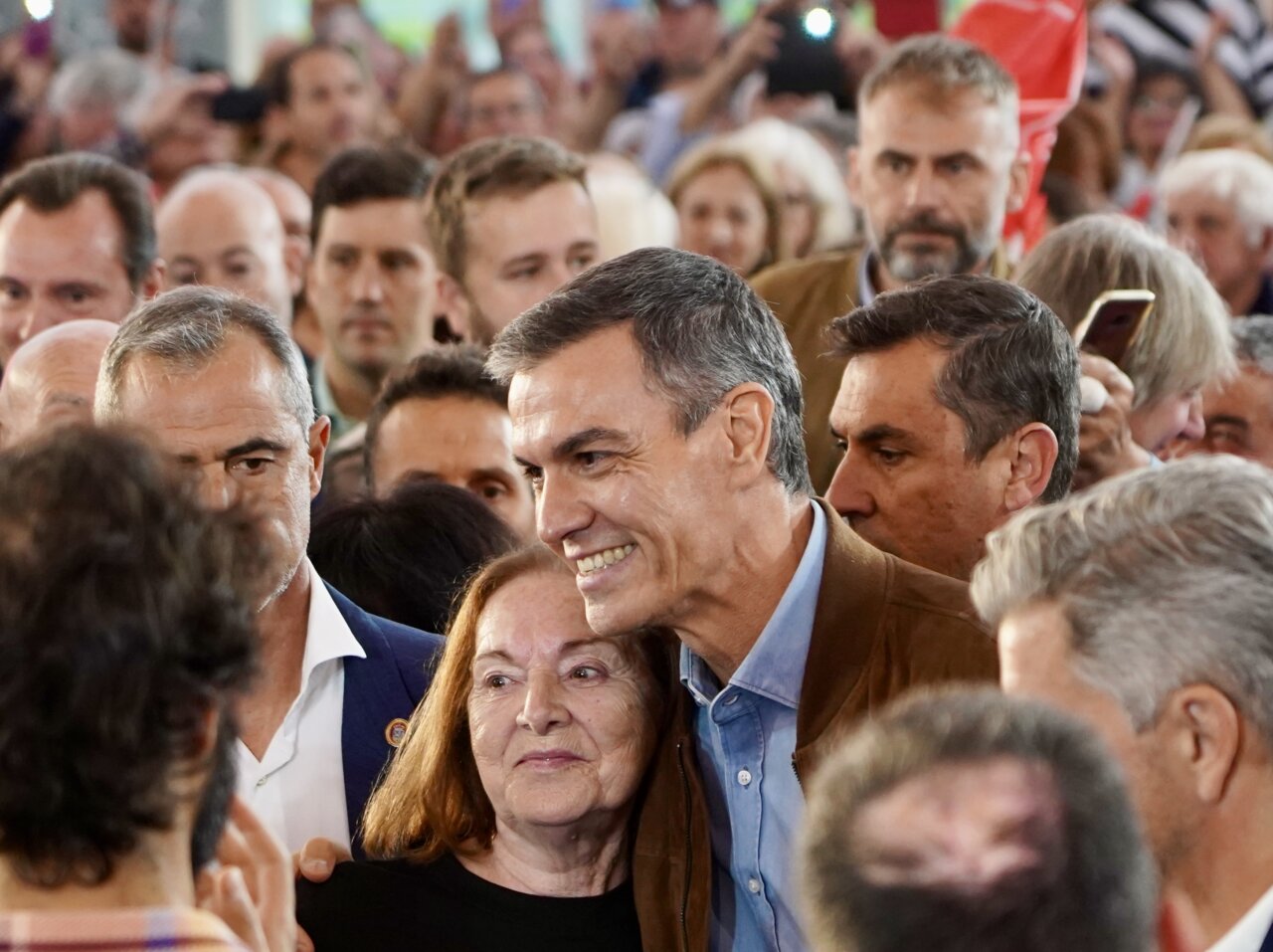 Pedro Sánchez posa junto a una mujer mientras varias personas los rodean en un acto.