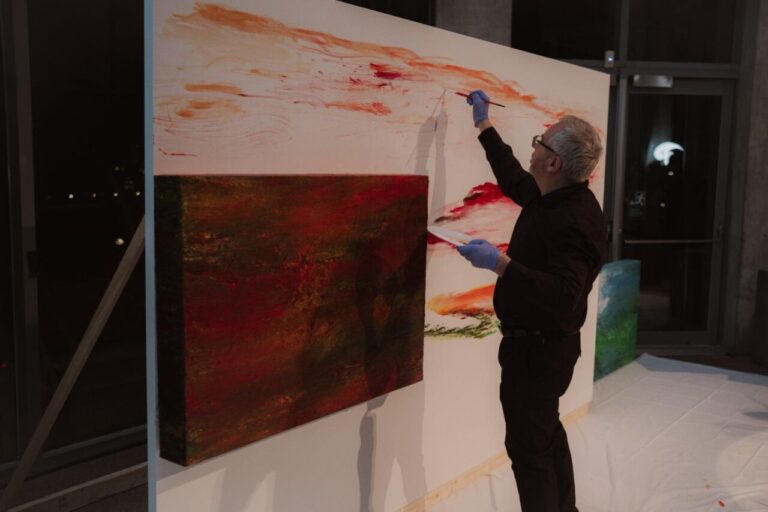 Una persona pinta trazos naranjas sobre un gran lienzo junto a otra obra abstracta.
