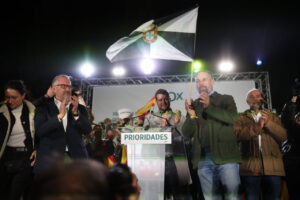 Varias personas aplauden en un escenario junto a un atril y una bandera