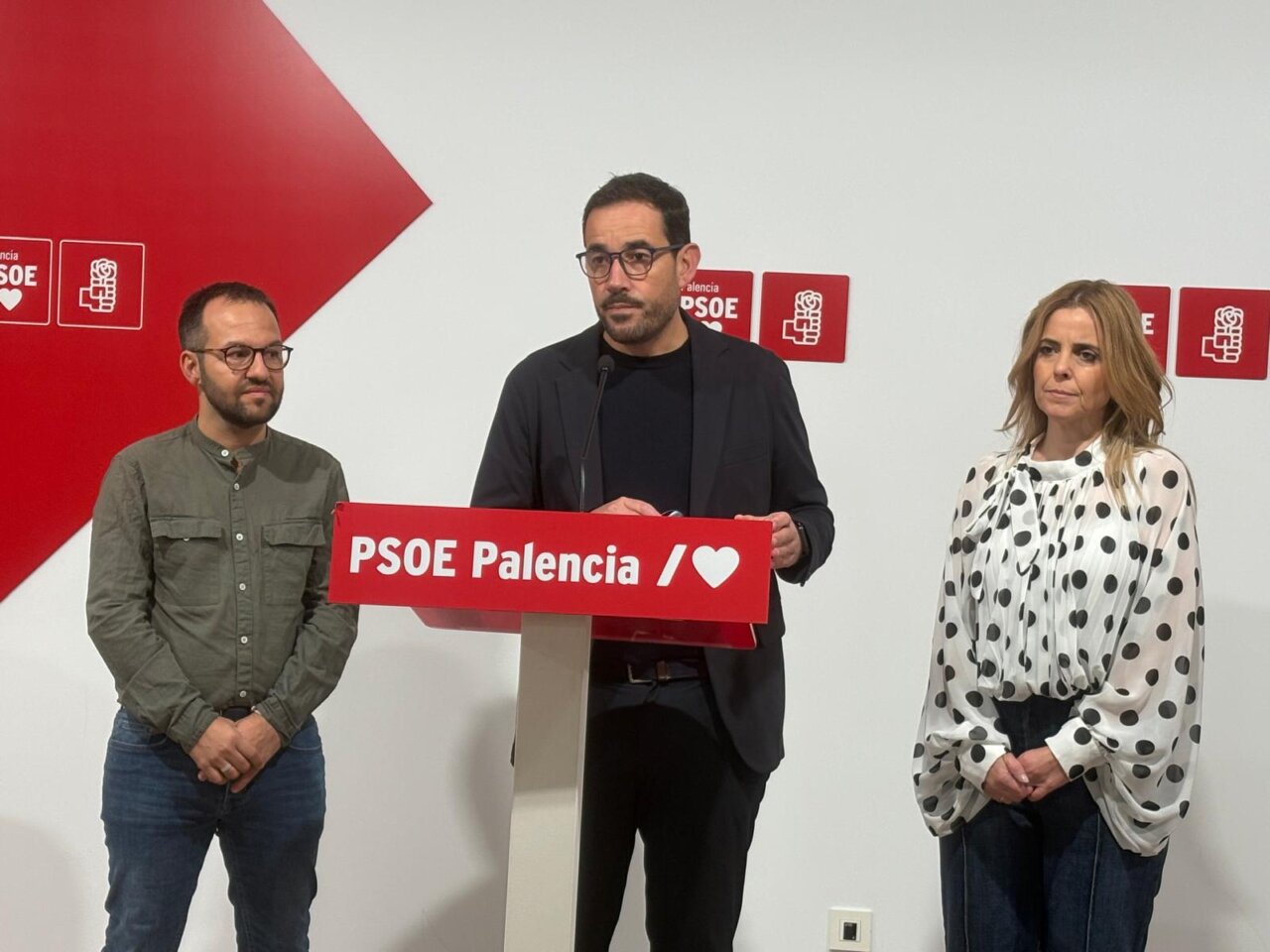 Tres personas junto a un atril del PSOE Palencia durante una comparecencia.