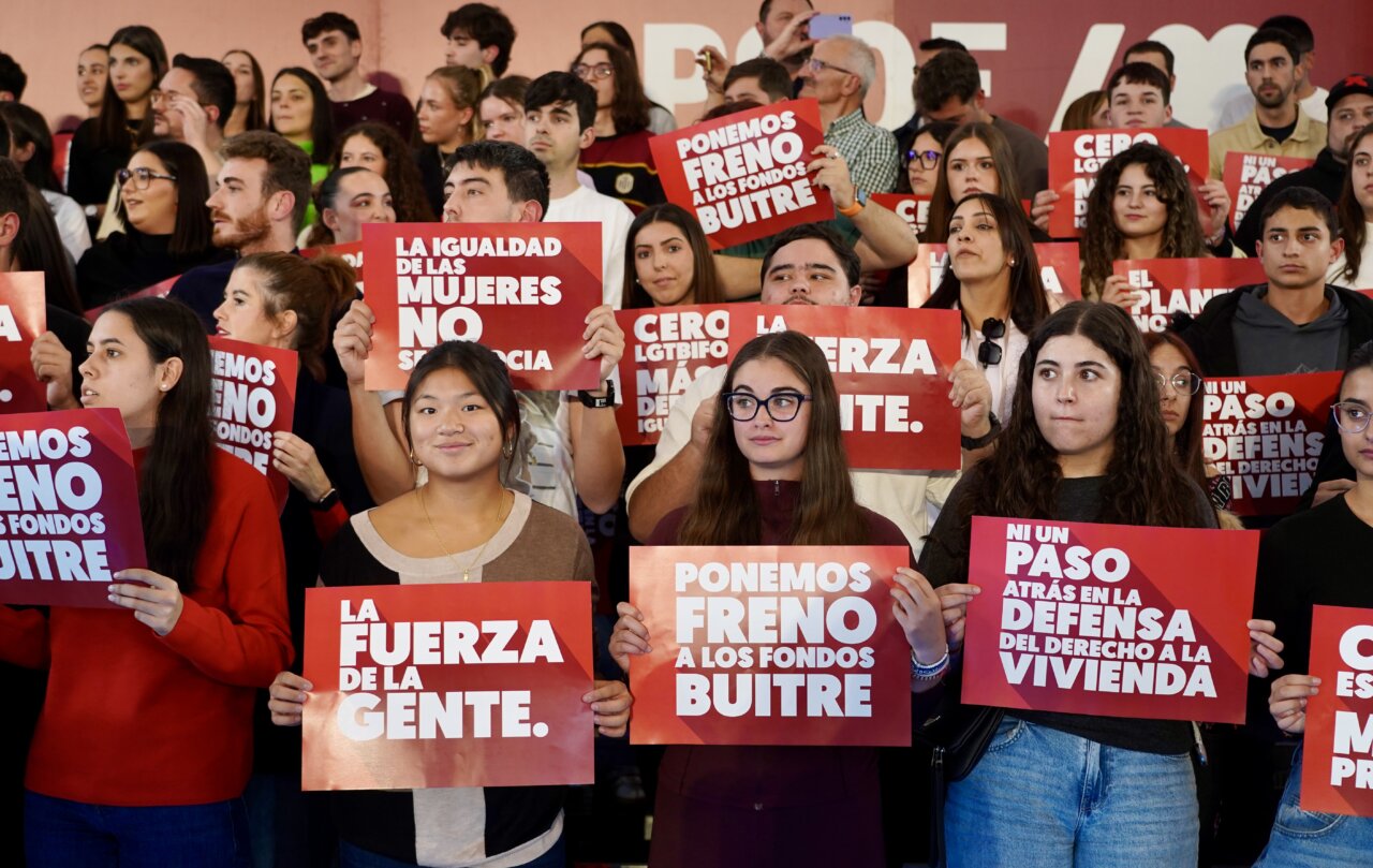 Varias personas sostienen carteles rojos con mensajes sobre vivienda, igualdad y fondos buitre.