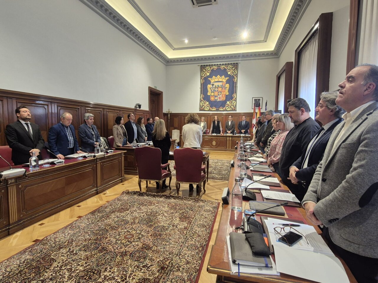 Personas de pie alrededor de una mesa larga en una sala institucional de reuniones