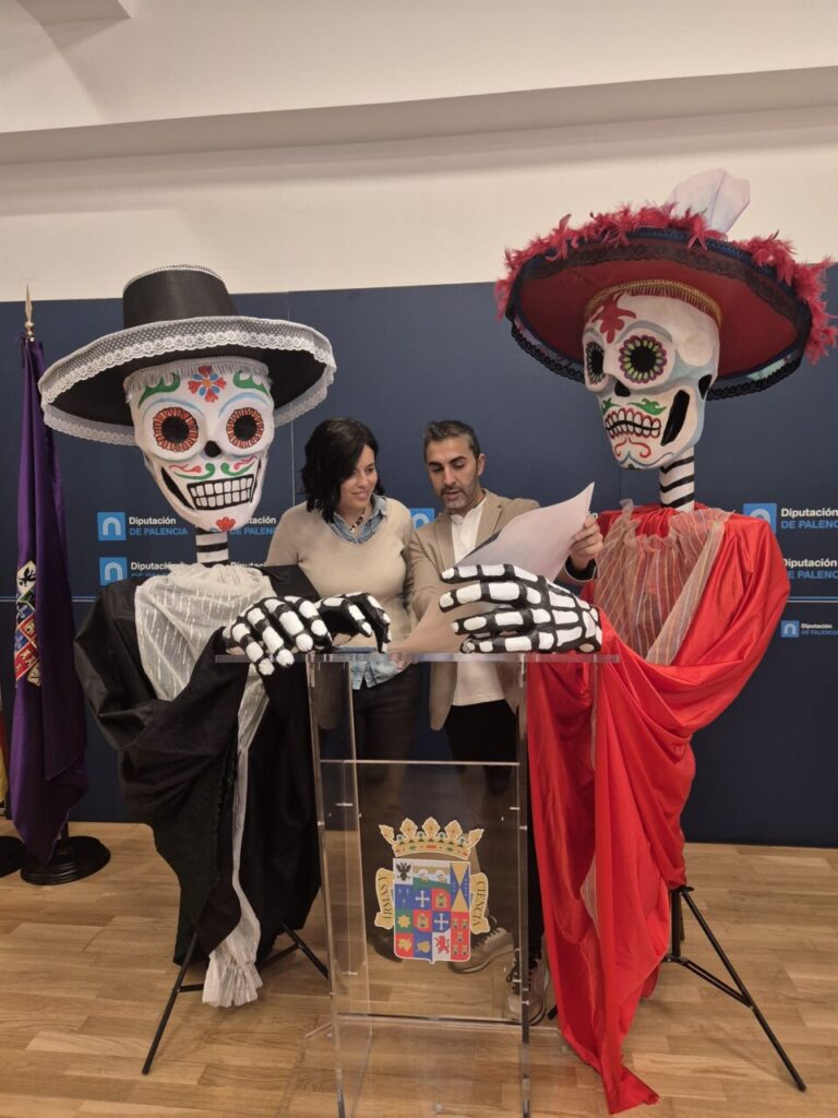Dos personas junto a figuras gigantes de esqueletos con trajes coloridos
