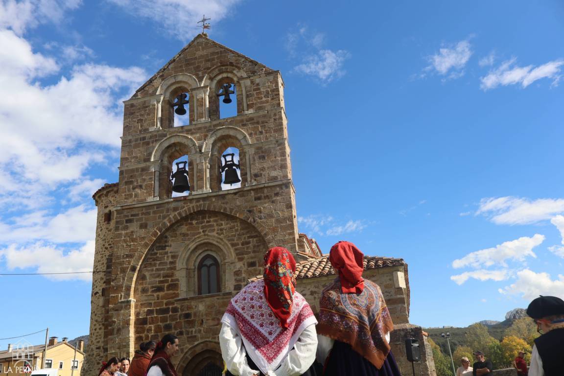 Personas con indumentaria tradicional frente a una iglesia de piedra con campanario.