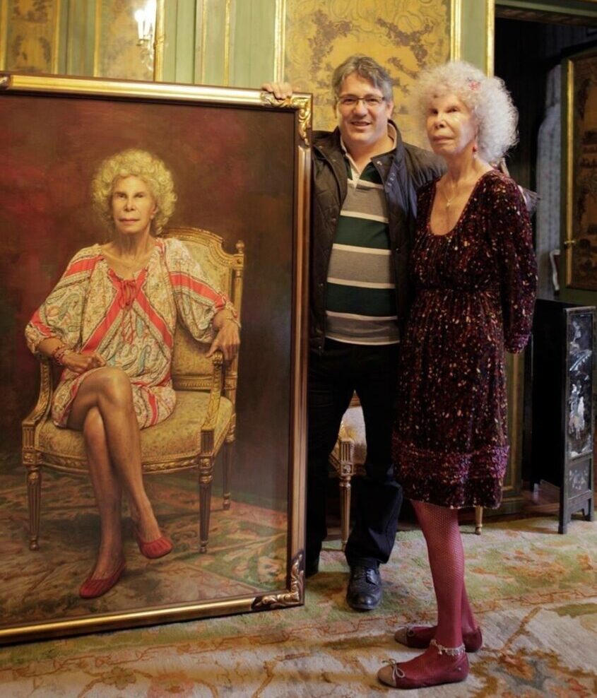 Dos personas posan junto a un gran retrato enmarcado de la duquesa de Alba.