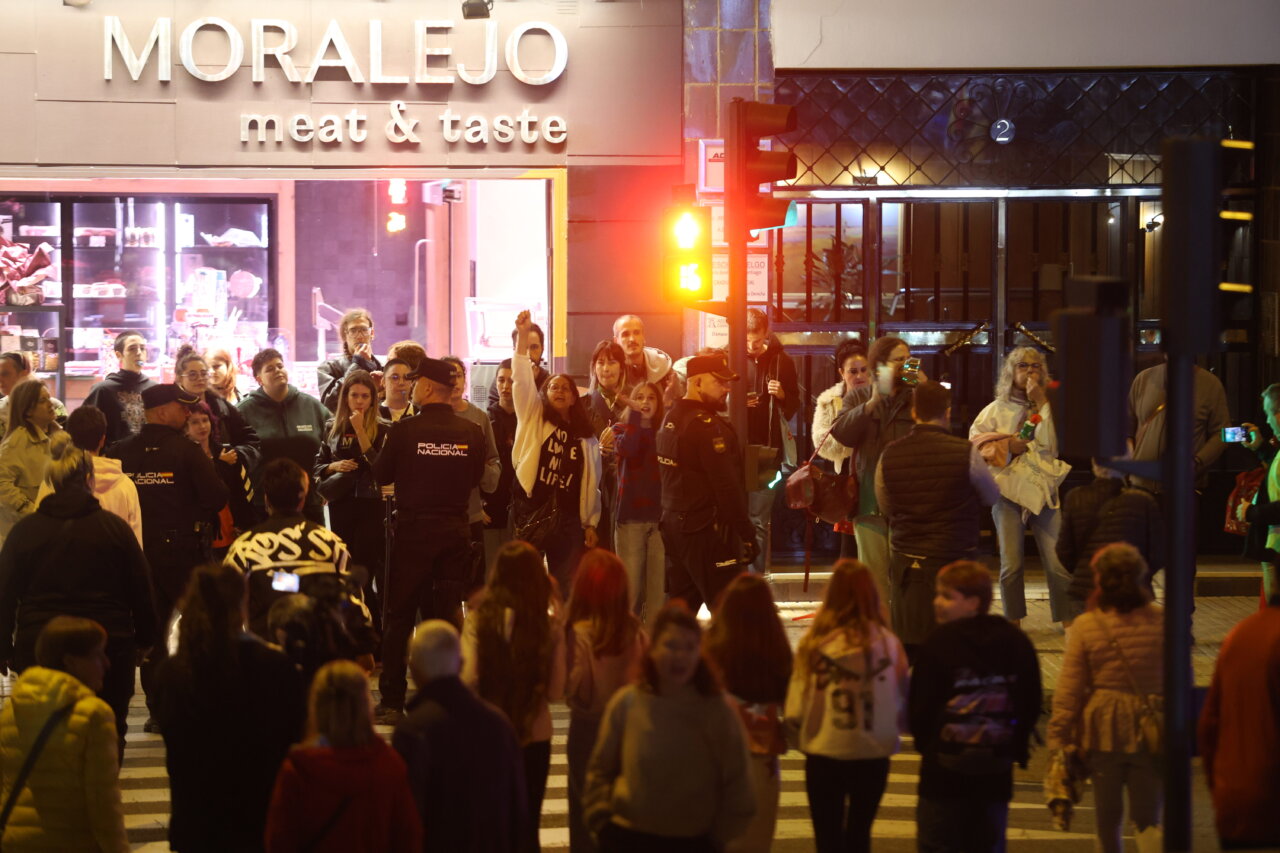 Grupo de personas y agentes de policía junto a un cruce peatonal iluminado de noche.