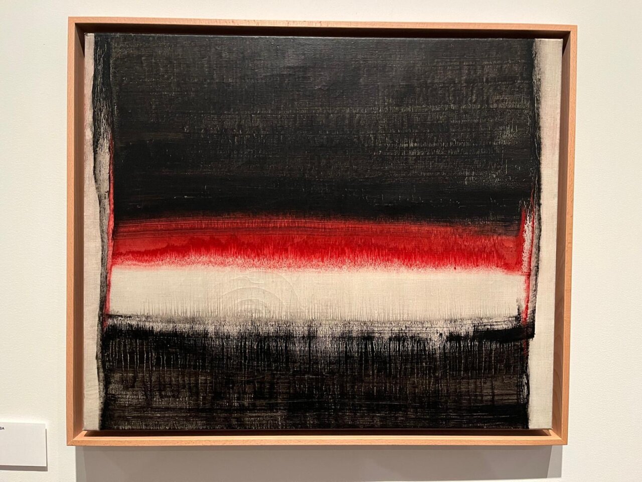 Pintura abstracta enmarcada con franjas negras, rojas y blancas expuesta en una pared.
