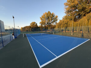 Pista de tenis azul al aire libre, con una persona junto a la valla.
