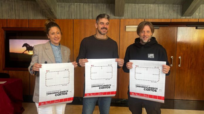 Tres personas sostienen carteles del festival Terroríficamente Cortos en una sala.