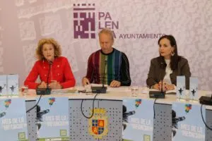 Tres personas sentadas ante micrófonos, con carteles del Mes de la Infancia en Palencia