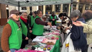 Personas con chalecos verdes atienden un puesto con productos rosas bajo una carpa de la asociación.
