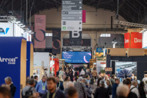 Visitantes recorren un recinto ferial gastronómico con puestos, señalización colgante y carteles de Barcelona.