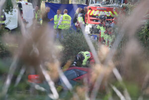 Un rescatista se inclina sobre un coche rojo parcialmente sumergido, con equipos de emergencia detrás.