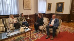 Cuatro personas sentadas conversan en un salón con muebles clásicos y alfombra