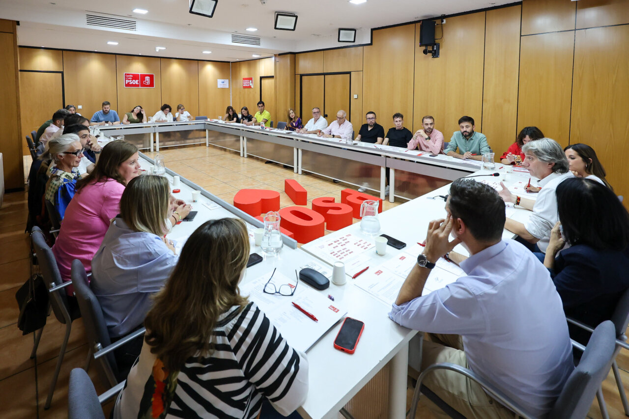 Personas reunidas alrededor de una mesa en una sala con carteles del PSOE.