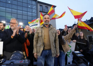 Un hombre en primer plano junto a asistentes con banderas españolas y de Vox.
