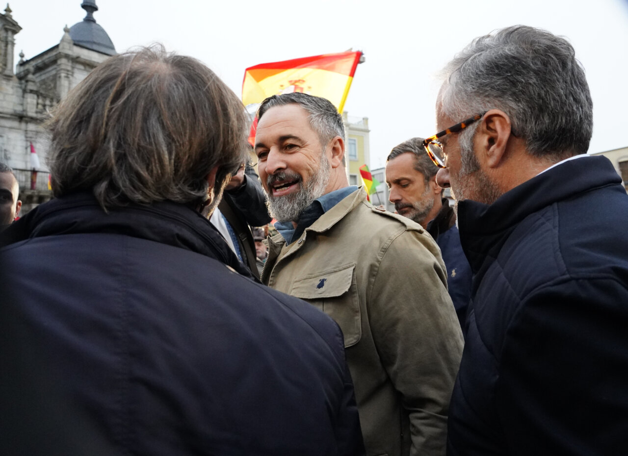 Santiago Abascal conversa con varias personas bajo banderas españolas en una plaza.