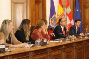 Varias personas sentadas ante una mesa larga en una sala institucional con banderas