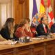 Varias personas sentadas ante una mesa larga en una sala institucional con banderas