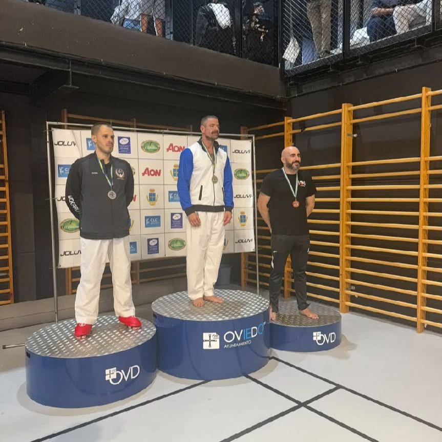 Tres hombres con medallas posan sobre un podio en un recinto deportivo