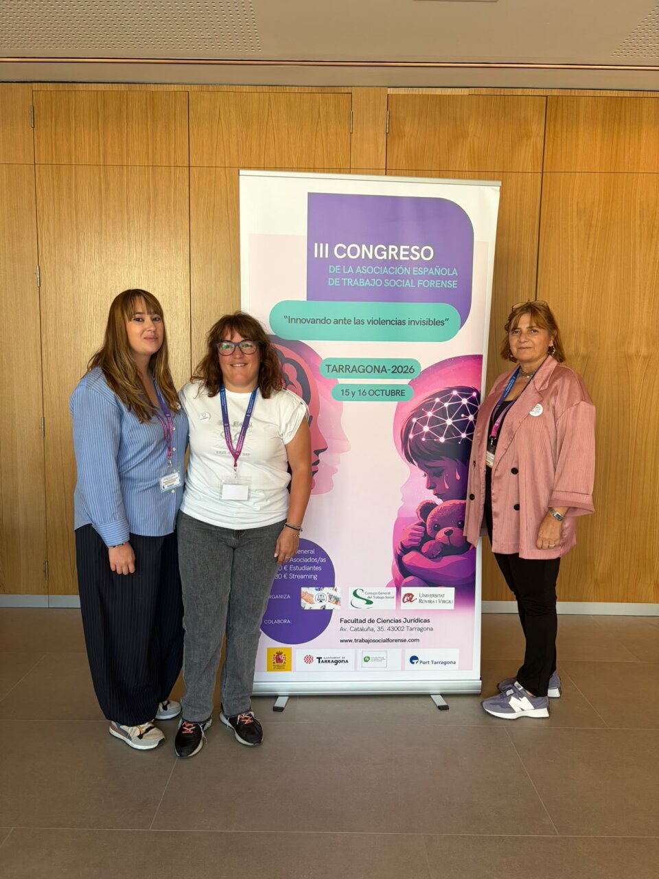Tres mujeres posan ante el cartel del III Congreso de Trabajo Social Forense.