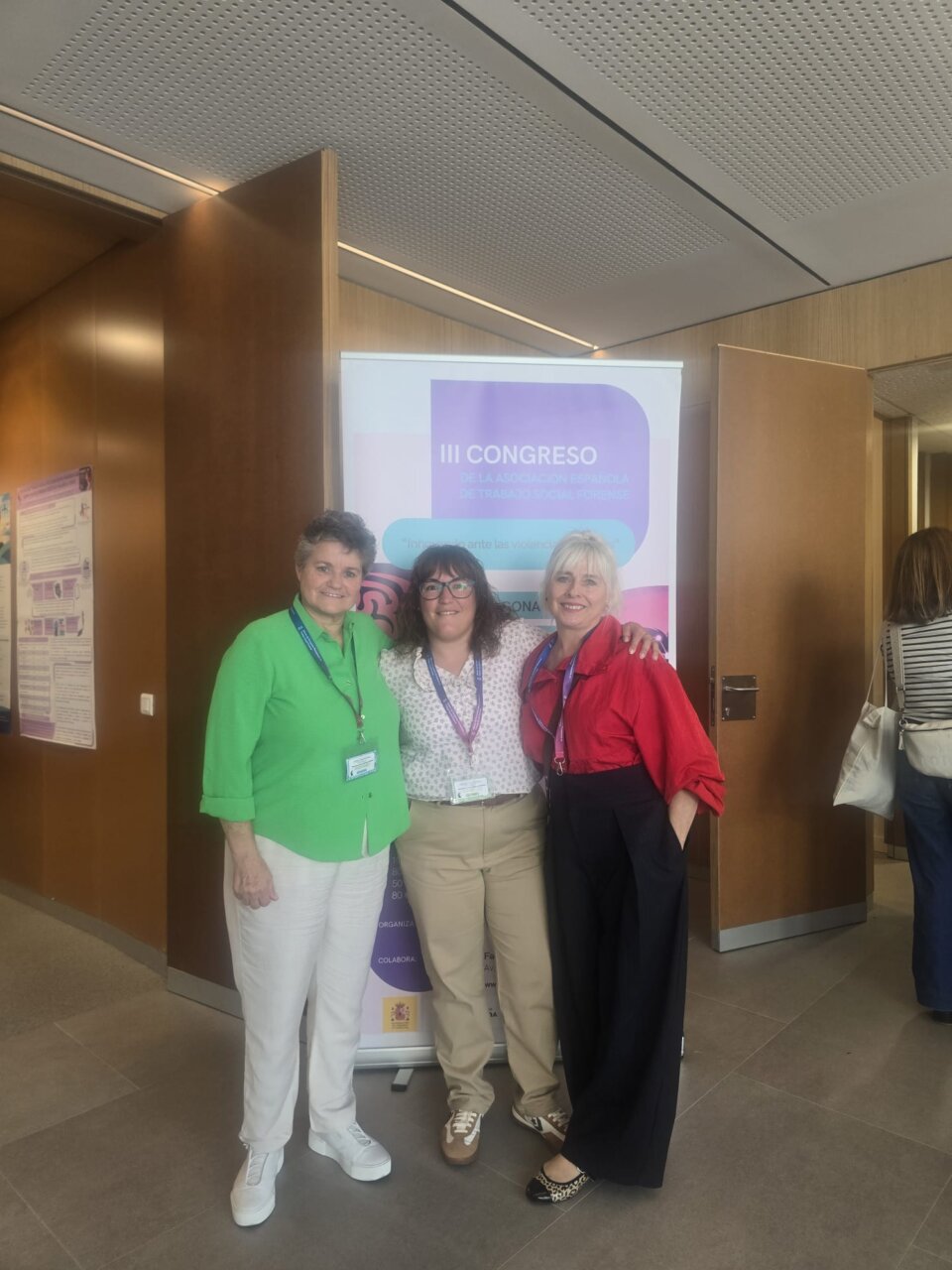 Tres mujeres posan ante un cartel del III Congreso de Trabajo Social Forense