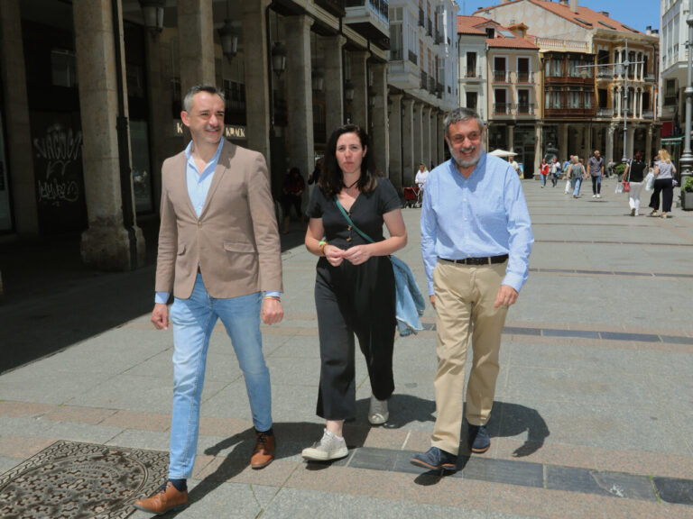 Tres personas caminan por una calle peatonal con edificios y soportales.