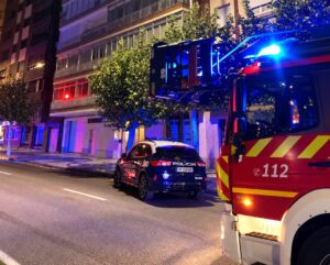 Vehículo policial y camión de bomberos estacionados de noche frente a un edificio.