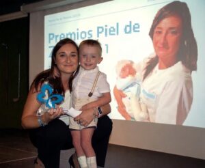 Una mujer sostiene un trofeo junto a un niño frente a una pantalla proyectada.